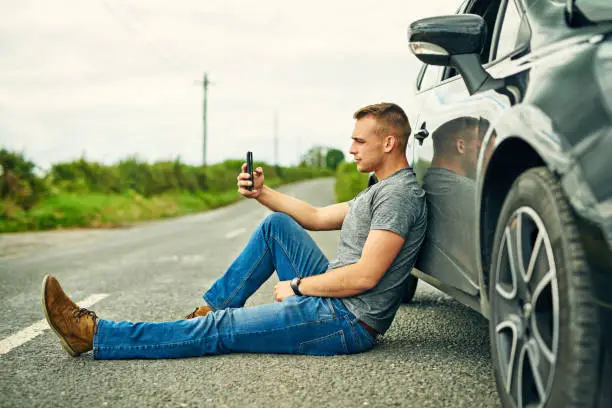 Shot of a young man waiting for roadside assistance after breaking down