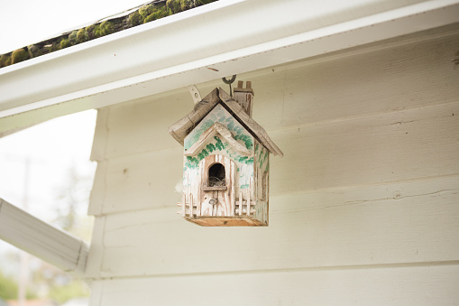 Small bird house hanging from the roof of a house or garage.