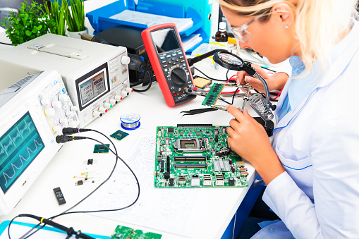Young attractive female digital electronic engineer checking green circuit board PCB in laboratory