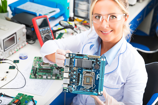 Young attractive smiling female digital electronic engineer holding computer PC motherboard in hands in the laboratory