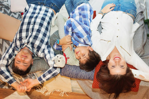 istock smiling young family with son looking at camera while lying together on bed. Happy young father, mother and cute child boy lying on bed 886465330