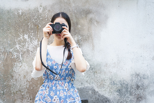beautiful woman holding camera against grey concrete wall.