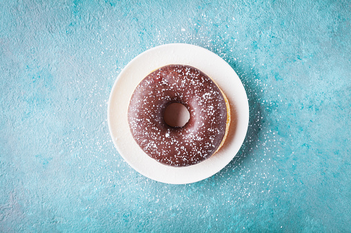 Chocolate donut or doughnut in plate on turquoise table top view. Flat lay.