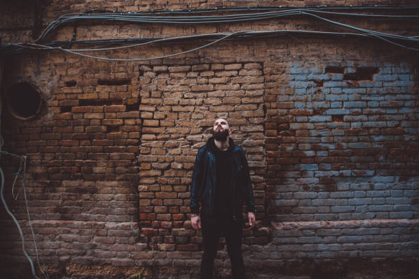 istock Modern young bearded man in black style clothes posing against brick wall. 886494930