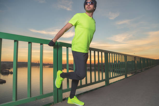 Urban jogger stretching on a bridge above the river in sunset / sunrise time.