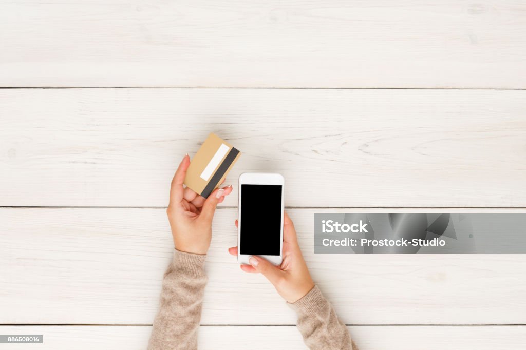 Online shopping in internet concept Online shopping in internet concept. Woman using credit card and blank smartphone, white wooden table background, top view Mobile Phone Stock Photo