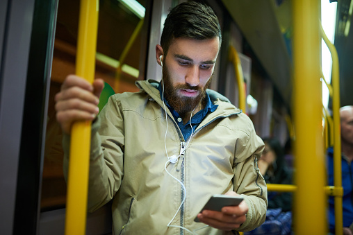 Cropped shot of a handsome young man listening to music on his cellphone while travelling on a bus