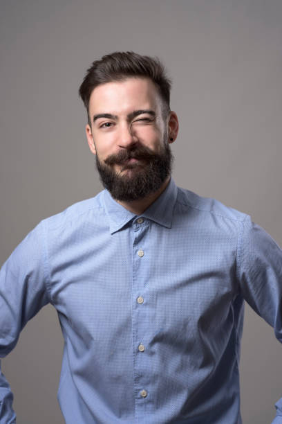 istock Childish young bearded hipster in formal wear winking with funny expression looking at camera 886533438