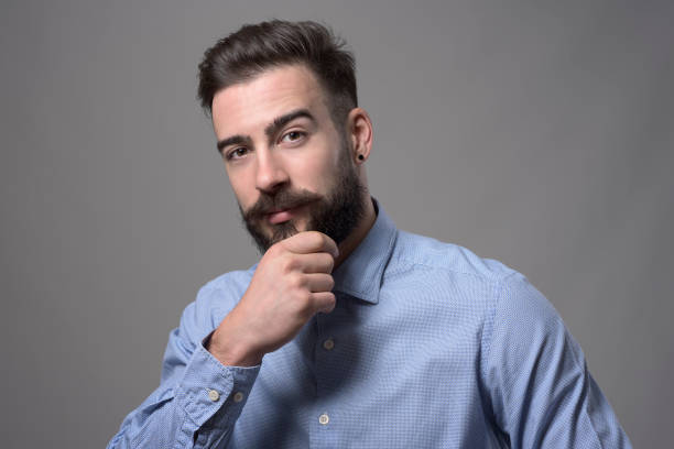 istock Successful young adult business man touching beard looking at camera thoughtfully 886533878