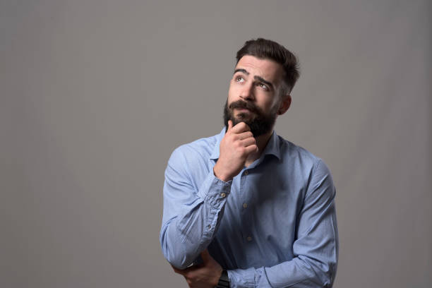 istock Young adult hipster business man thinking and looking up at copyspace while touching beard 886534230