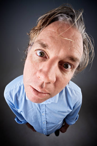 A middle-aged man, distorted by use of a fisheye lens, looks goofily at camera, his head tilted and his eyes wide.