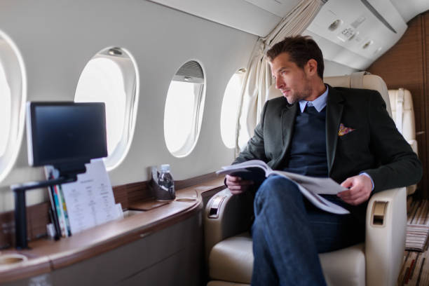 Man in private jet airplane Man sitting inside private jet airplane and looking outside the window while reading a magazine. ceo photos stock pictures, royalty-free photos & images