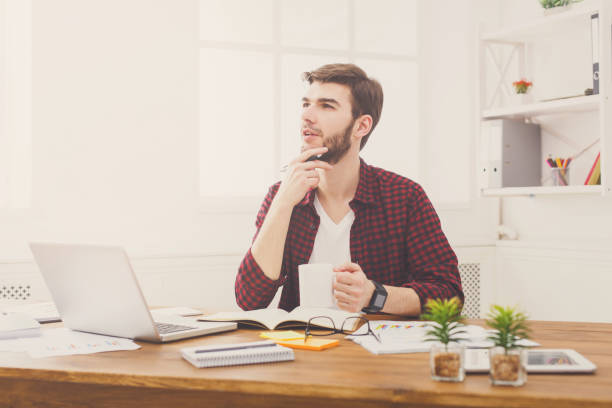 istock Pensive young businessman with laptop in modern white office 886563792