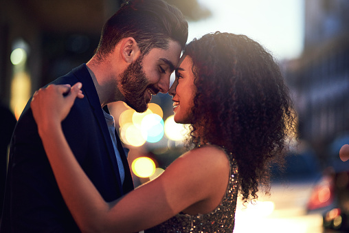 Shot of a cheerful young couple holding one another while looking into each other's eyes outside at night