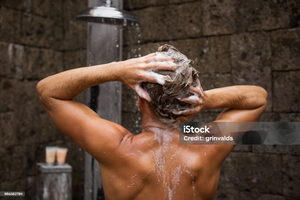 Man washing hair in shower Man washing hair in shower, photo taken from back. Men Stock Photo