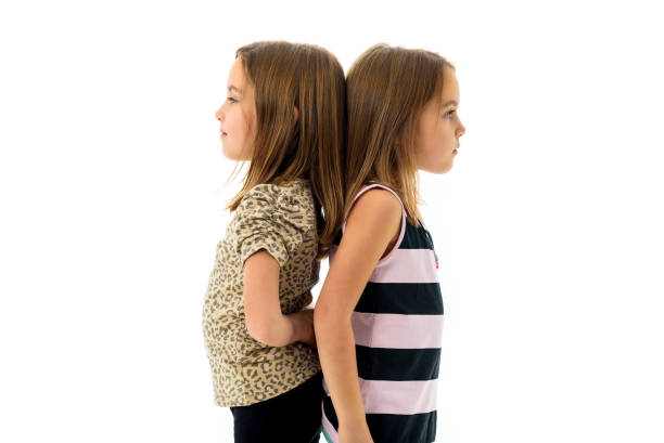 istock Identical twin girls are turned facing back to back. 886619854