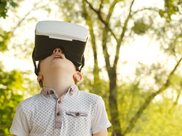 istock Boy in a virtual reality helmet on a background of green forest. 886624606