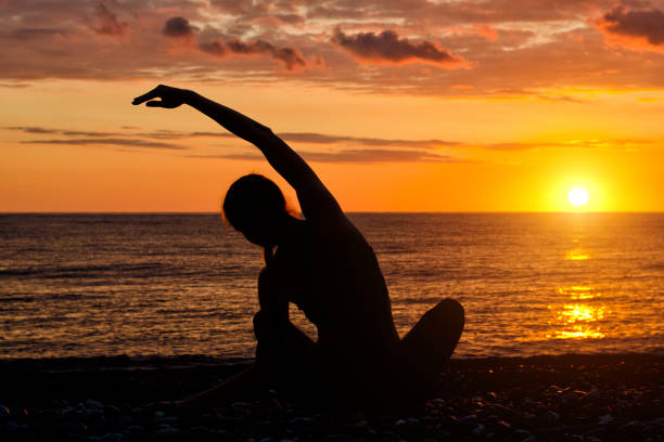 istock Girl practicing yoga on the beach. View from the back, sunset, silhouettes 886625336