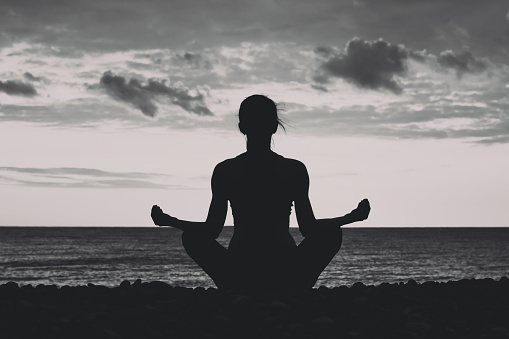 Woman meditating on the beach in lotus position. Silhouette, black and white