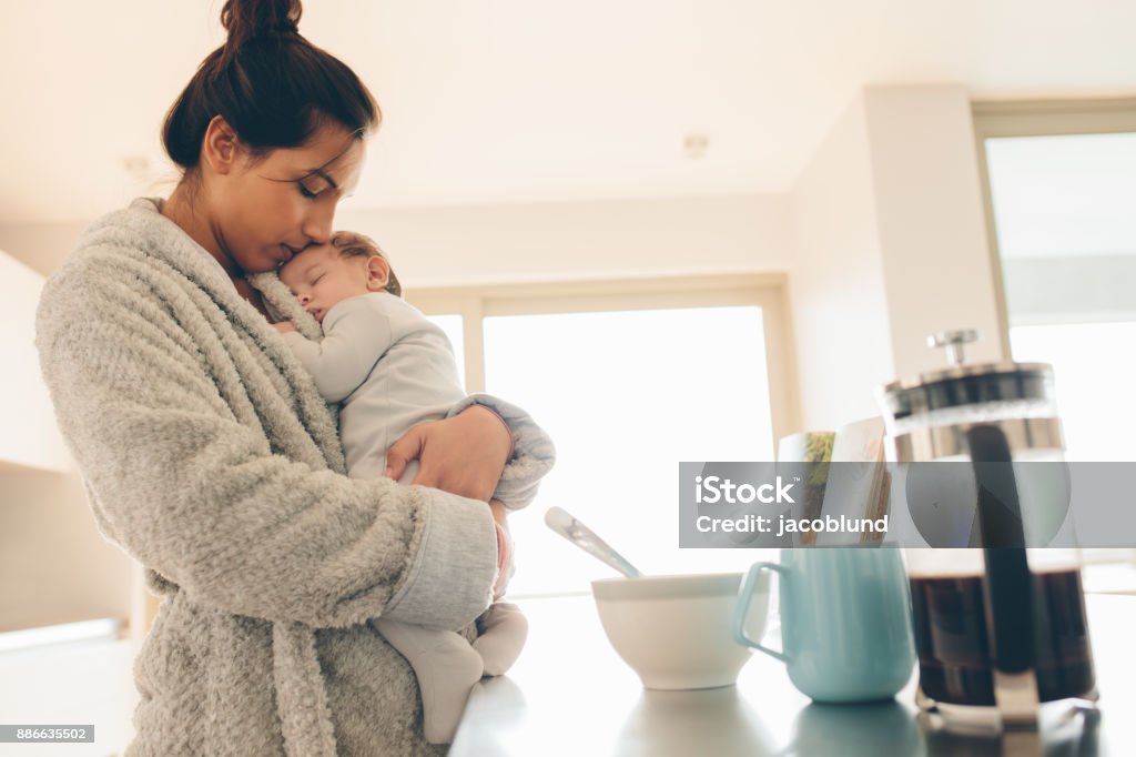 Little boy sleeping in his mother's arms Little boy sleeping in his mother's arms. Woman wearing bathrobe carrying her son in kitchen. Mother Stock Photo