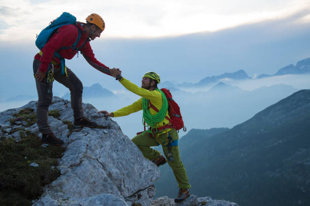 istock Man helping friend to climb rock mountain 886635834