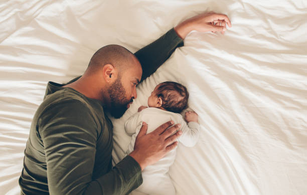 Newborn baby boy sleeping with his father on bed Top view of newborn baby boy sleeping with his father on bed. Father and son lying together on bed. lifestyle newborn stock pictures, royalty-free photos & images
