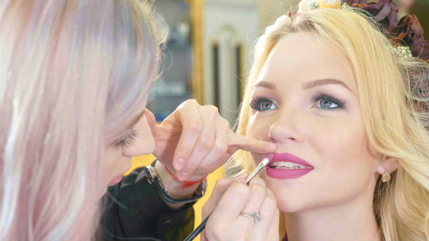 istock Young makeup artist applying lipstick on model's lips. 886661712