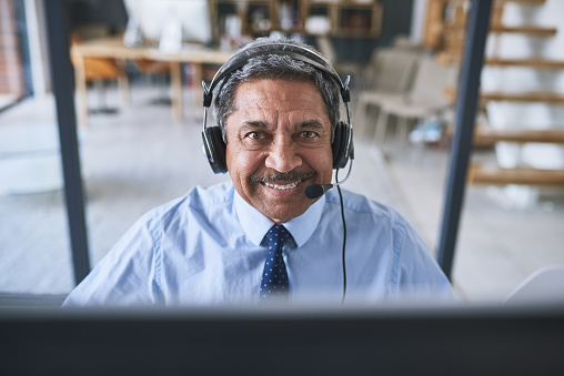 Portrait of a cheerful businessman talking to a customer using a headset while looking at the camera