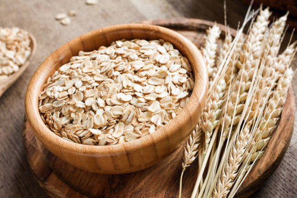 Rolled oats or oat flakes and golden wheat ears on wooden background. stock photo