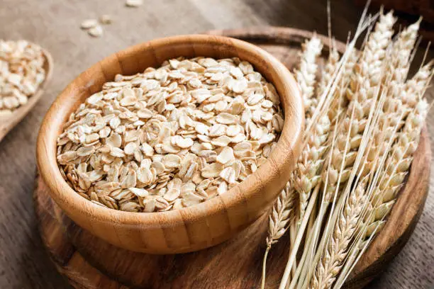 Rolled oats or oat flakes and golden wheat ears on wooden background. Concept of agriculture, healthy eating, healthy lifestyle