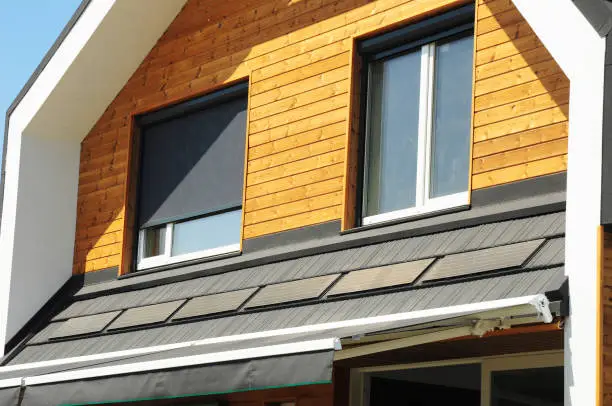 Photo of House Blinds Sun Protection Exterior with Solar Panels. Windows in New Modern Passive House Attic Facade Wooden Wall with Shutters Closed and Opened Outdoors.