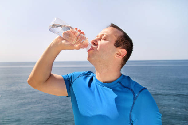 istock An athlete making a break during training, drinking fresh clean water from a bottle, rests and enjoys the clean air, with a beautiful blue sky and the sea in the background. Healthy lifestyle concept. 886680510