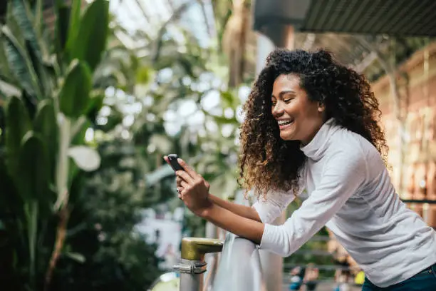 Photo of Adorable dark skinned woman with afro hairstyle using her phone.