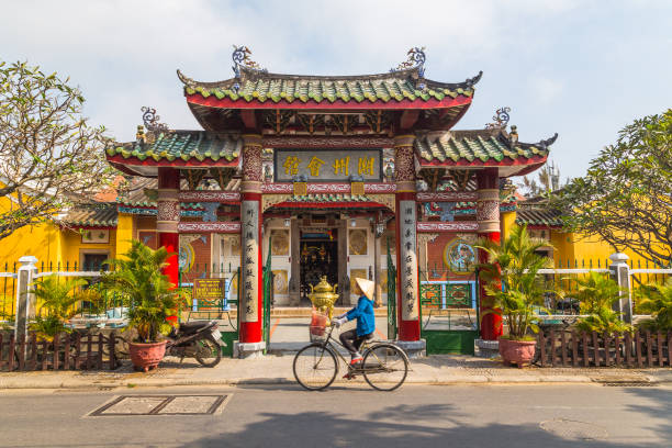 Trieu Chau Assembly Hall in Hoi An Vietnam The outside of the Trieu Chau Assembly Hall in Hoi An, Vietnam during the day. A person with a traditional conical hat can be seen going past on a bike. hoi an stock pictures, royalty-free photos & images