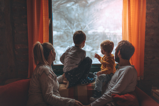 Portrait of a young family with two little boys, and third one on the way, being surprised by snow, early in the morning - right after waking up