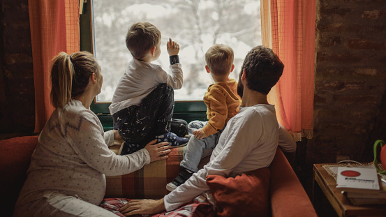 Portrait of a young family with two little boys, and third one on the way, being surprised by snow, early in the morning - right after waking up // wide photo dimensions