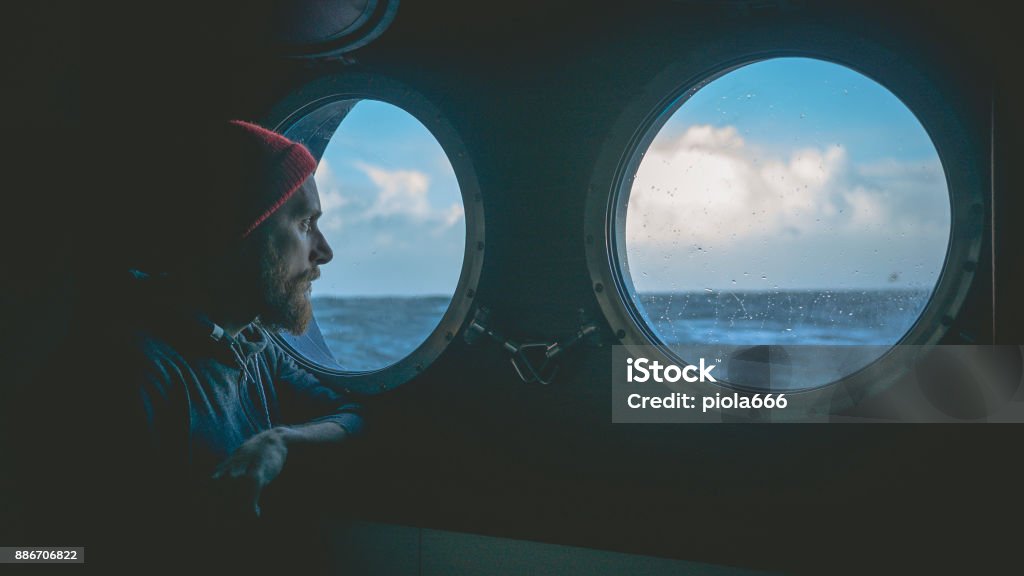 Man at the porthole window of a vessel in a rough sea Sea Stock Photo