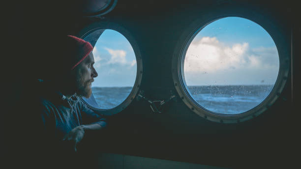 Man at the porthole window of a vessel in a rough sea Man at the porthole window of a vessel in a rough sea fishing boat photos stock pictures, royalty-free photos & images