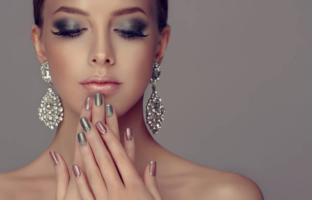 Stylish manicure and make up in a silver color. Beautiful woman-model dressed in a big silver earings is showing silver and rose manicure on the nails and rose lipstick on the lips. Fashion makeup and cosmetic. fingernail photos stock pictures, royalty-free photos & images