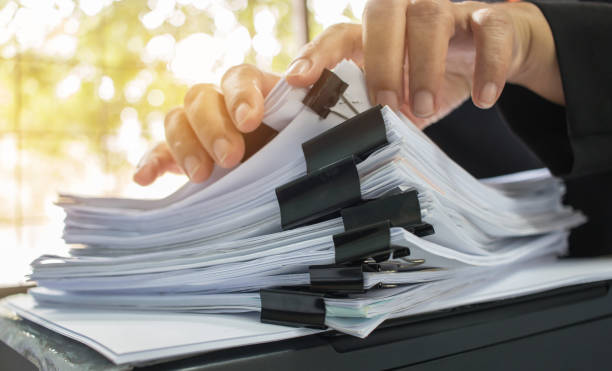 istock Businessman hands working in Stacks of document paper files for searching information on work desk office, business report papers or documents achieves with clip paper. 886745580