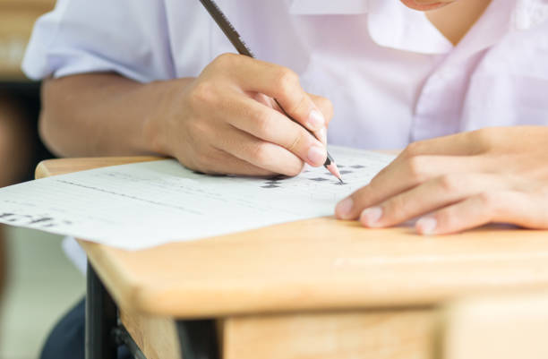 istock Asian Boy Students taking exams, writing examination room with undergraduate students inside. Student sitting learning lessons on row desk chair doing final exam in classroom with uniform. 886746264