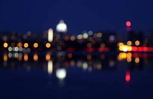 Silhouette of Madison skyline at night with out of focus street lights and glowing in the dark state Capitol building reflected in a lake water during twilight. Wisconsin, Midwest USA.