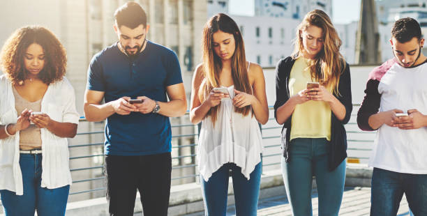 We live in a technology-based society Cropped shot of a group of young people texting on their cellphones while standing outdoors image based social media photos stock pictures, royalty-free photos & images