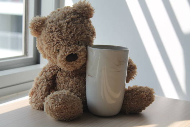istock Bear toy with cup sitting by the window in shadows 886804586