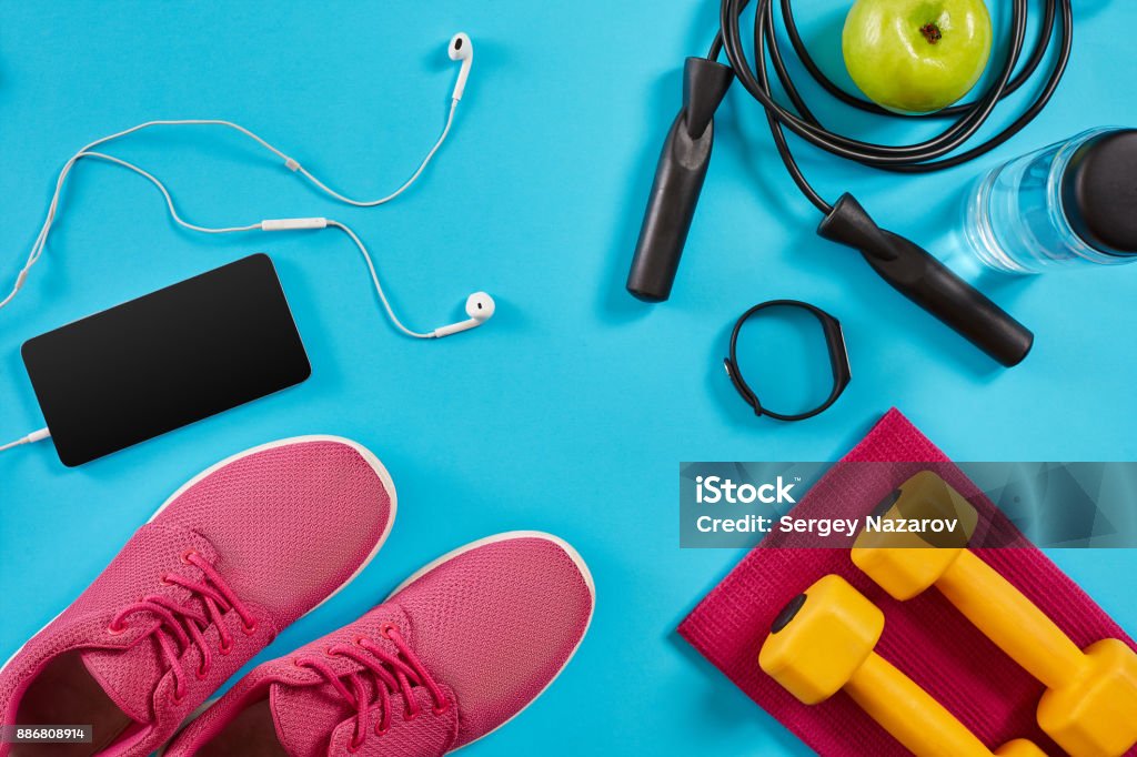 Flat lay shot of sneakers, jumping rope, dumbbells and smartphone on blue background Flat lay shot of sneakers, jumping rope, dumbbells and smartphone on blue background. Active lifestyle, body care concept. Top view. Copy space. Flat lay. Still life Portable Information Device Stock Photo