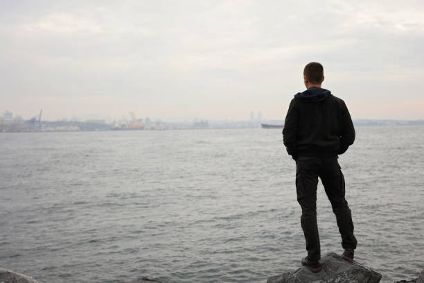istock Man standing near the sea and looking at horizon, cloudy windy day. Thinking, Concentration, Loneliness concept. 886819002