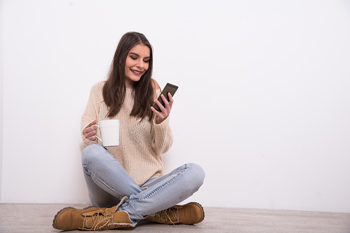 An attractive young woman is seen sitting on the floor and looking at the mobile phone.