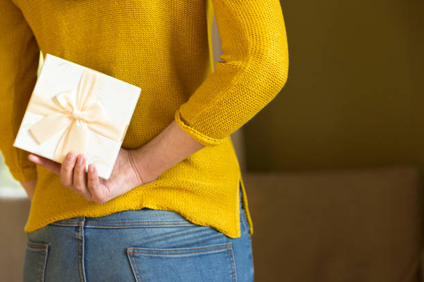 Woman hiding gift box behind her back stock photo