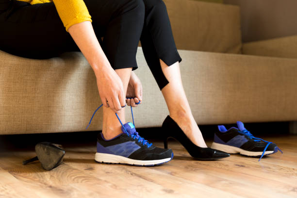 mujer cambiantes tacones altos, zapatos de la oficina después de la jornada sentado en el sofá, dispuesta a dar un paseo o correr - afterwork business fotografías e imágenes de stock