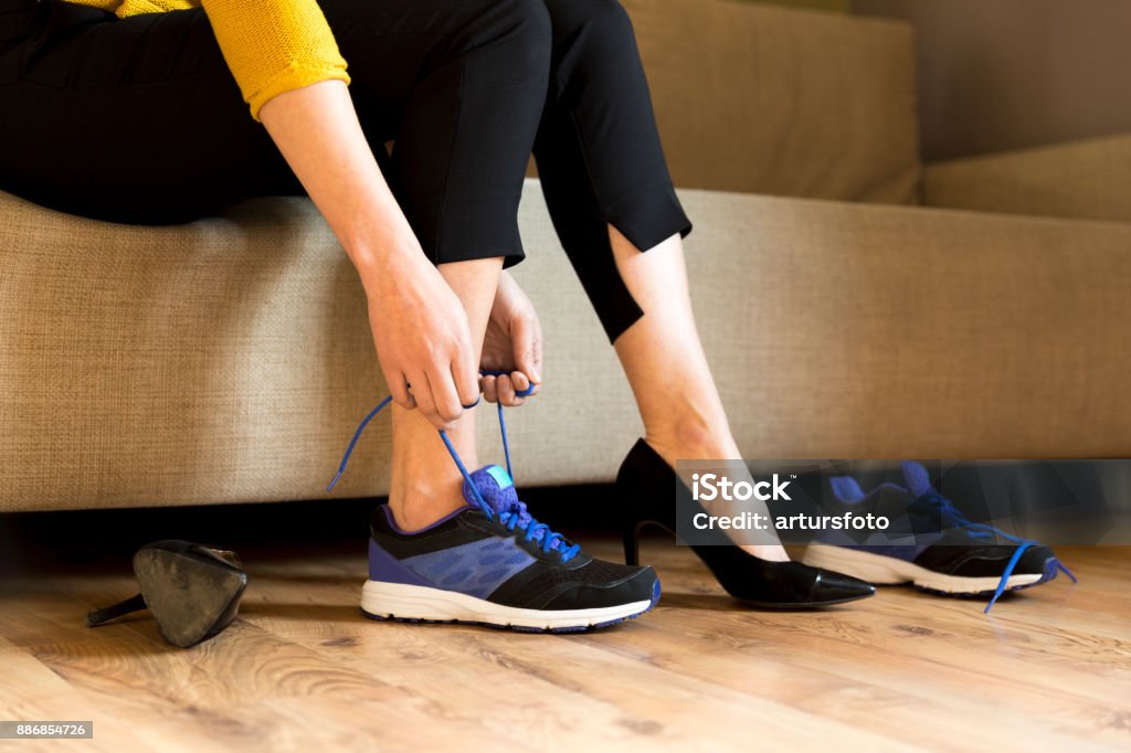 Woman changing high heels, office shoes after working day while sitting on the couch, ready to take a walk or run Shoe Stock Photo